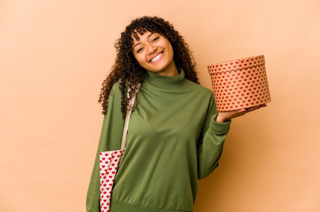 Jeune femme afro-américaine afro-américaine tenant un cadeau de Saint Valentin heureux, souriant et joyeux.