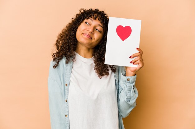 Jeune femme afro-américaine afro-américaine tenant une carte de Saint Valentin rêvant d'atteindre les objectifs et buts