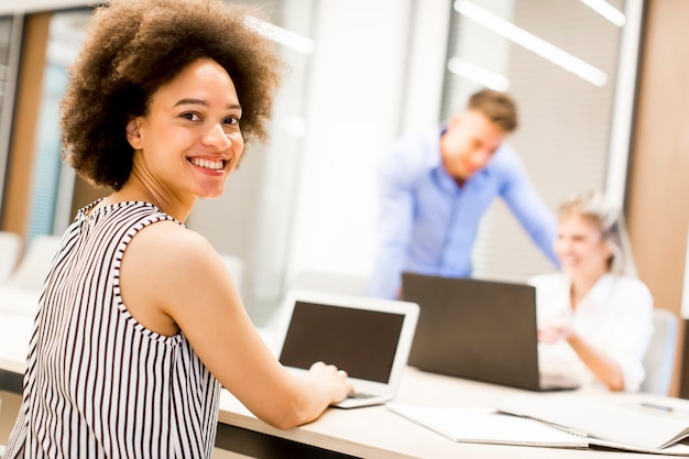 Jeune femme afro-américaine assis et utilisant un ordinateur portable dans un bureau moderne