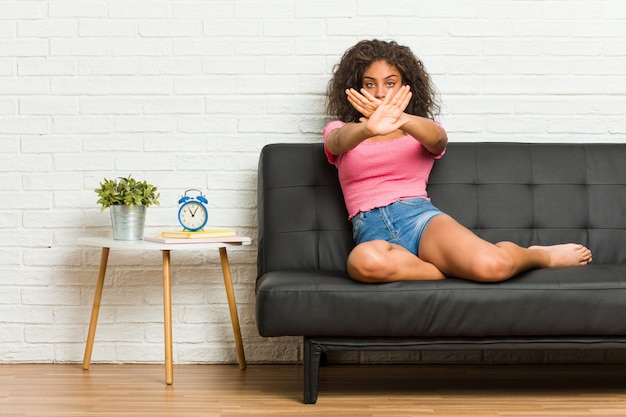 Jeune femme afro-américaine assise sur le canapé en faisant un geste de déni