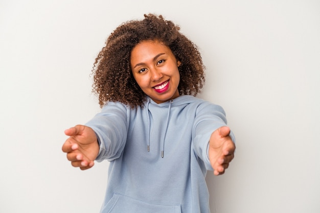 Jeune femme afro-américaine aux cheveux bouclés isolé sur fond blanc montrant une expression de bienvenue.