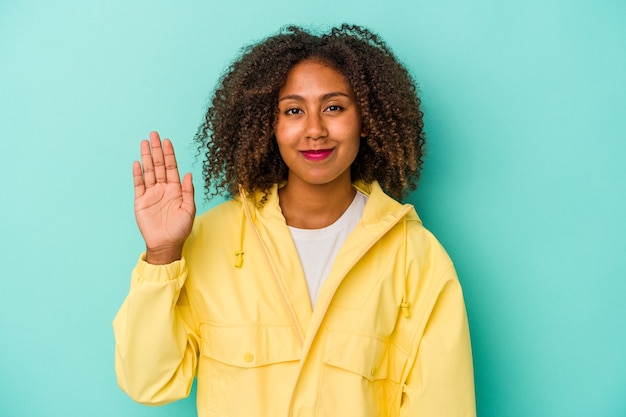 Jeune femme afro-américaine aux cheveux bouclés isolé sur fond bleu souriant joyeux montrant le numéro cinq avec les doigts.