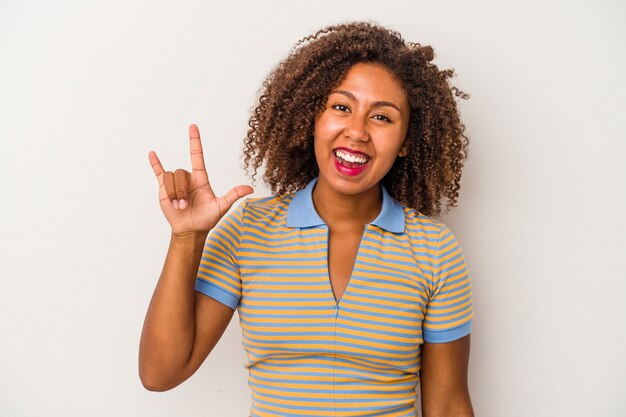 Jeune femme afro-américaine aux cheveux bouclés isolée sur fond blanc montrant un geste de cornes comme concept de révolution.