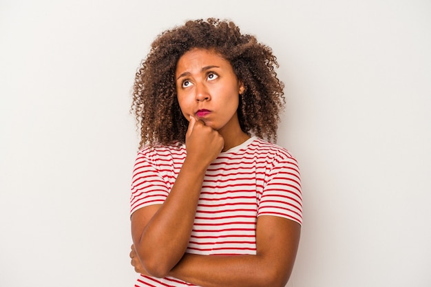 Jeune femme afro-américaine aux cheveux bouclés isolée sur fond blanc pensant et levant, réfléchissant, contemplant, ayant un fantasme.