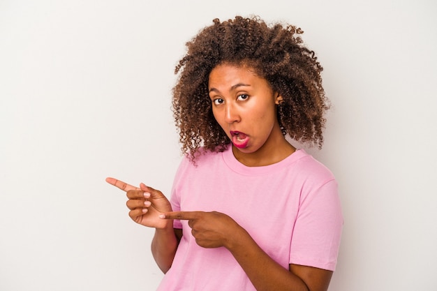 Jeune femme afro-américaine aux cheveux bouclés isolée sur fond blanc pointant avec les index vers un espace de copie, exprimant l'excitation et le désir.