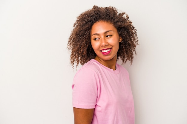 Jeune femme afro-américaine aux cheveux bouclés isolée sur fond blanc regarde de côté souriante, gaie et agréable.