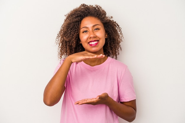 Jeune femme afro-américaine aux cheveux bouclés isolée sur fond blanc tenant quelque chose à deux mains, présentation du produit.