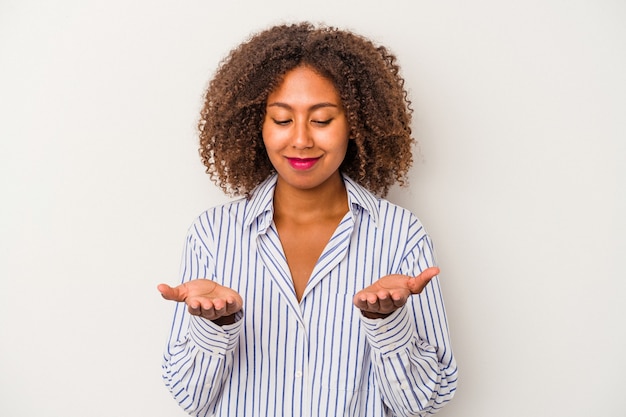 Jeune femme afro-américaine aux cheveux bouclés isolée sur fond blanc tenant quelque chose avec des paumes, offrant à la caméra.