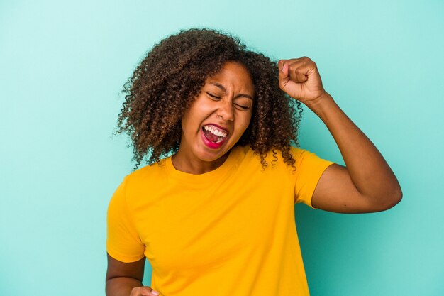 Jeune femme afro-américaine aux cheveux bouclés isolée sur fond bleu applaudissant insouciante et excitée. Notion de victoire.