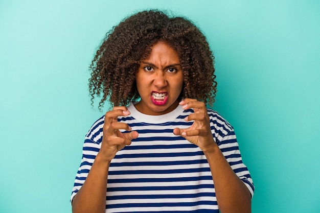 Jeune femme afro-américaine aux cheveux bouclés isolée sur fond bleu contrariée en criant avec les mains tendues.