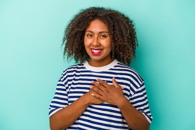 Jeune femme afro-américaine aux cheveux bouclés isolée sur fond bleu a une expression amicale, appuyant la paume sur la poitrine. Notion d'amour.