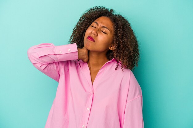 Jeune femme afro-américaine aux cheveux bouclés isolée sur fond bleu fatiguée et très endormie en gardant la main sur la tête.