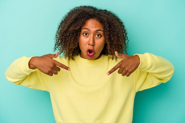 Jeune femme afro-américaine aux cheveux bouclés isolée sur fond bleu pointe vers le bas avec les doigts, sentiment positif.