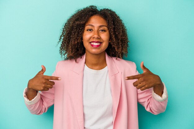 Jeune femme afro-américaine aux cheveux bouclés isolée sur fond bleu pointe vers le bas avec les doigts, sentiment positif.