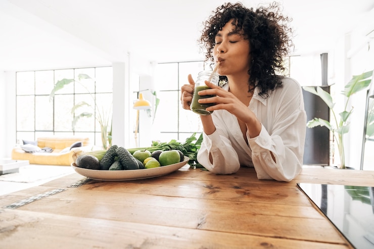Photo jeune femme afro-américaine buvant du jus vert avec de la paille de bambou réutilisable dans un loft. notion de maison. concept de mode de vie sain. espace de copie