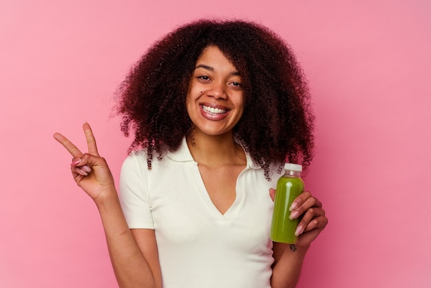 Jeune femme afro-américaine buvant un smoothie sain isolé sur rose montrant le numéro deux avec les doigts.