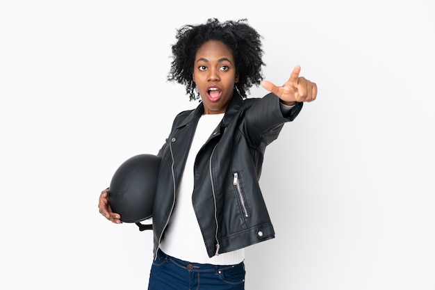 Jeune femme afro-américaine avec un casque de moto isolé sur mur blanc pointant loin