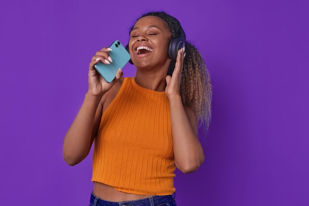 Une jeune femme afro-américaine chante en tenant un téléphone portable au lieu d'un microphone.