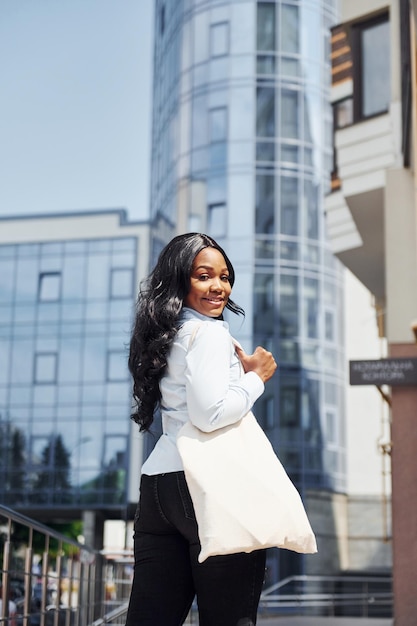 Jeune femme afro-américaine en chemise blanche à l'extérieur de la ville contre le bâtiment de l'entreprise