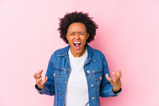 Jeune femme afro-américaine contre un fond rose isolé criant de rage.