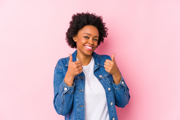 Jeune femme afro-américaine contre un fond rose isolé soulevant les deux pouces vers le haut, souriant et confiant.