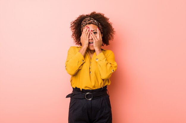 Jeune femme afro-américaine contre un mur rose cligner des doigts effrayés et nerveux.