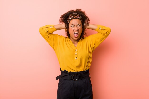 Jeune femme afro-américaine contre un mur rose couvrant les oreilles avec les mains essayant de ne pas entendre le son trop fort.