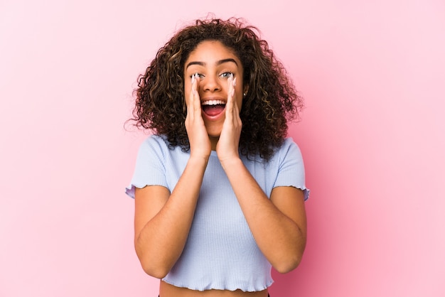 Jeune femme afro-américaine contre un mur rose criant excité à l'avant.