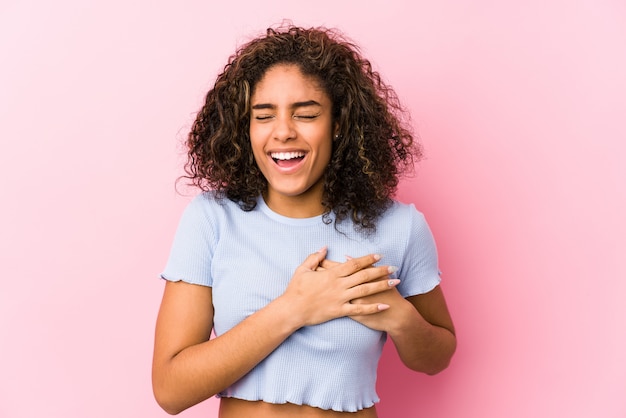 Jeune femme afro-américaine contre un mur rose en riant en gardant les mains sur le cœur, le concept du bonheur.