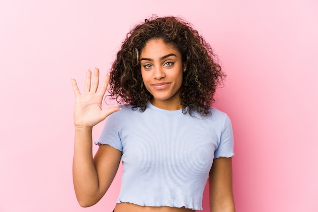 Jeune femme afro-américaine contre un mur rose souriant joyeux montrant le numéro cinq avec les doigts.