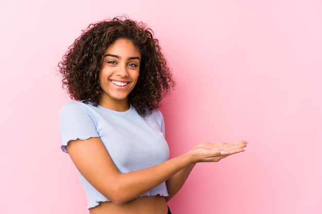 Jeune femme afro-américaine contre un mur rose tenant un espace copie sur une paume.