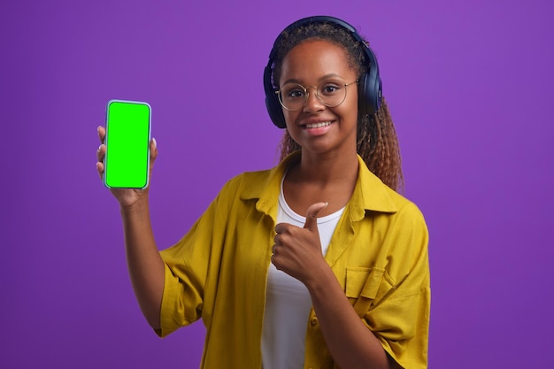 Jeune femme afro-américaine dans les écouteurs tenant le téléphone et montrant les pouces vers le haut