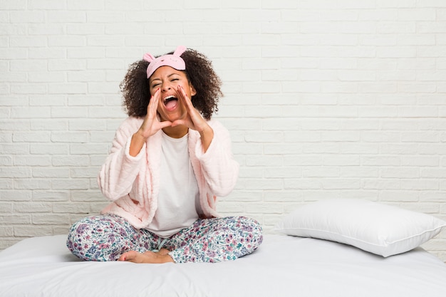 Jeune femme afro-américaine dans le lit portant des cris de pijama excités à l'avant.