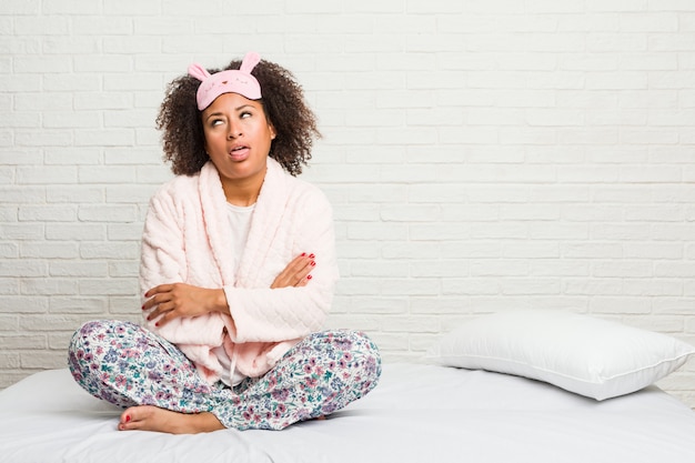 Jeune femme afro-américaine dans le lit portant un pijama fatigué d'une tâche répétitive.