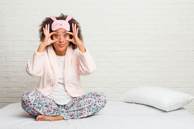 Jeune femme afro-américaine dans le lit portant un pijama en gardant les yeux ouverts pour trouver une opportunité de réussite.