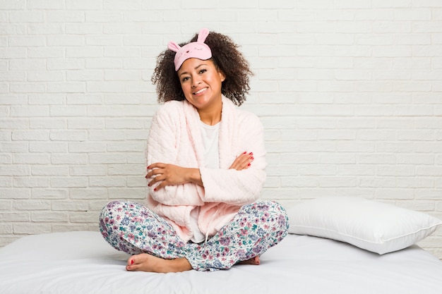 Jeune femme afro-américaine dans le lit portant un pijama qui se sent confiant, croisant les bras avec détermination.