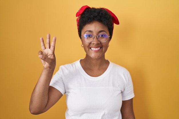 Photo jeune femme afro-américaine debout sur fond jaune montrant et pointant vers le haut avec les doigts numéro trois tout en souriant confiant et heureux.