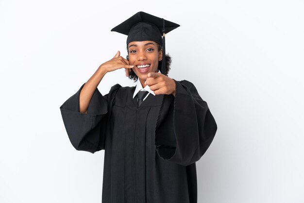 Jeune femme afro-américaine diplômée d'université isolée sur fond blanc faisant un geste de téléphone et pointant vers l'avant