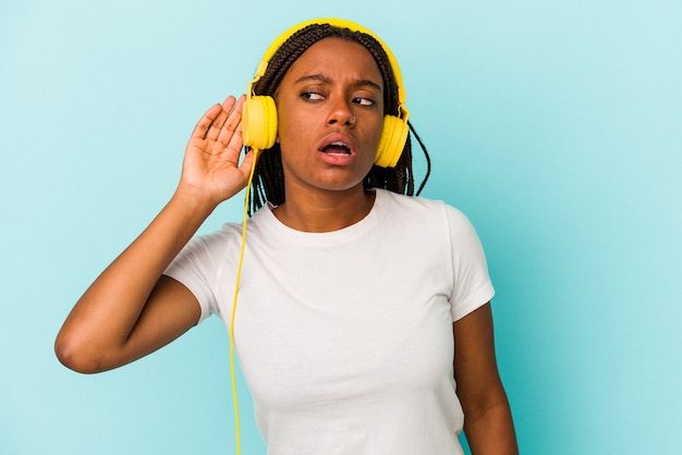 Photo jeune femme afro-américaine écoutant de la musique isolée sur fond bleu essayant d'écouter un potin.