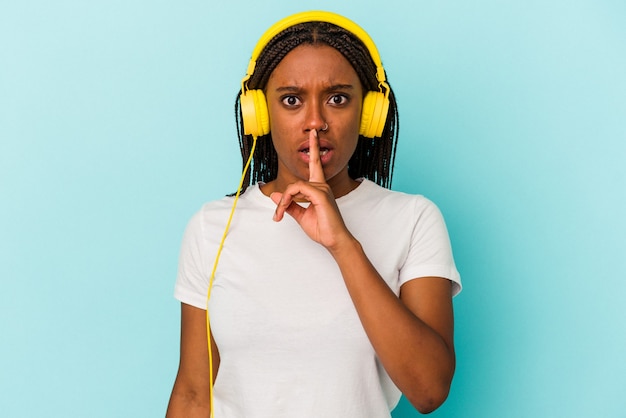 Jeune femme afro-américaine écoutant de la musique isolée sur fond bleu gardant un secret ou demandant le silence.