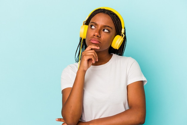 Jeune femme afro-américaine écoutant de la musique isolée sur fond bleu regardant de côté avec une expression douteuse et sceptique.