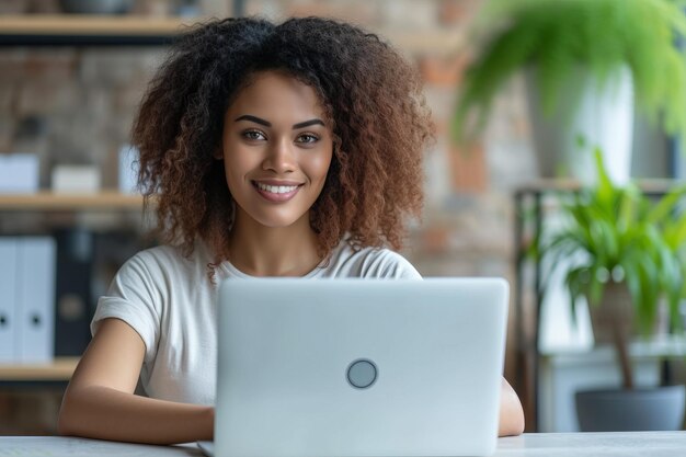 Une jeune femme afro-américaine est assise à son bureau et sourit tout en utilisant son ordinateur portable