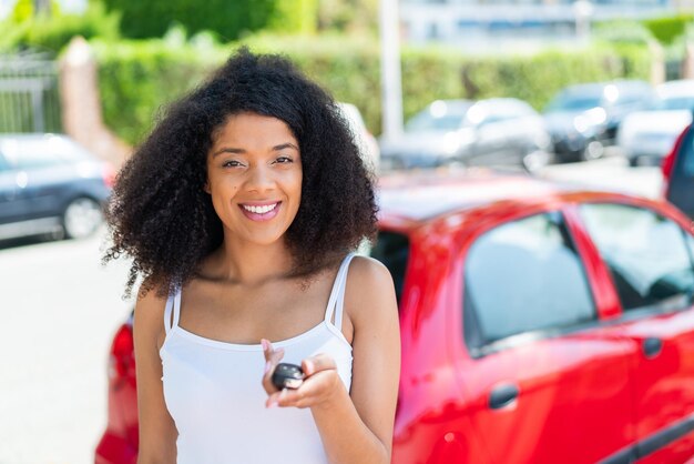 Une jeune femme afro-américaine à l'extérieur tenant les clés de la voiture avec une expression heureuse