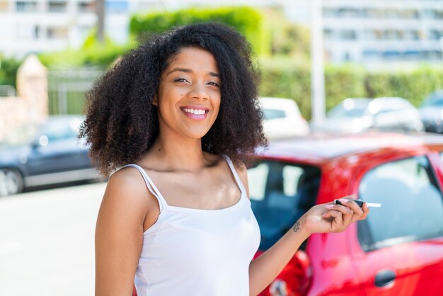 Une jeune femme afro-américaine à l'extérieur tenant les clés de la voiture avec une expression heureuse
