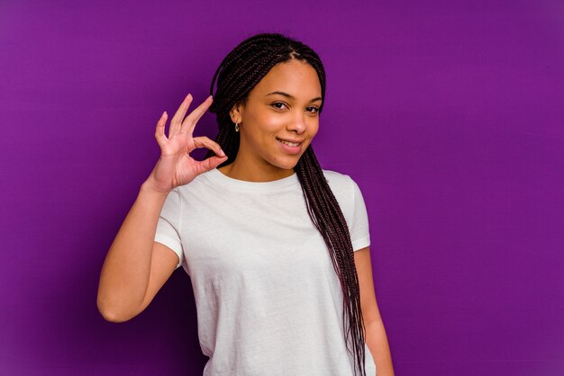 Jeune femme afro-américaine fait un clin d'œil et tient un bon geste avec la main.
