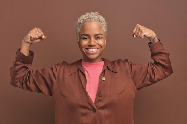 Jeune femme afro-américaine forte lève les bras pour montrer les muscles se tient en studio