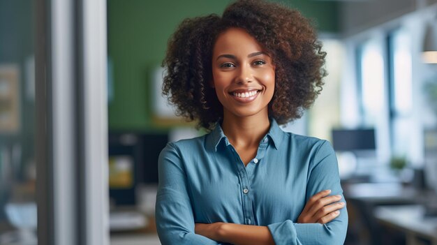 Une jeune femme afro-américaine heureuse debout avec les bras croisés dans le bureau.