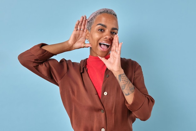 Une jeune femme afro-américaine heureuse met la paume à la bouche et l'oreille se tient dans le studio