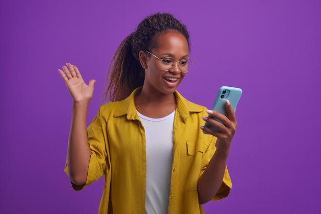 Jeune femme afro-américaine heureuse avec téléphone agitant la main et disant bonjour