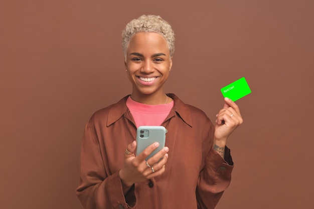 Jeune femme afro-américaine heureuse tenant un téléphone et exhibant une carte bancaire